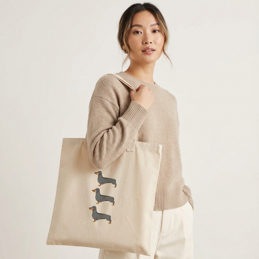 Woman holding a beige tote bag with dachshund design on a plain background